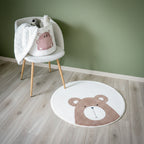 Et rundt hvitt teppe med en bamse, sammen med en stol med barneleker