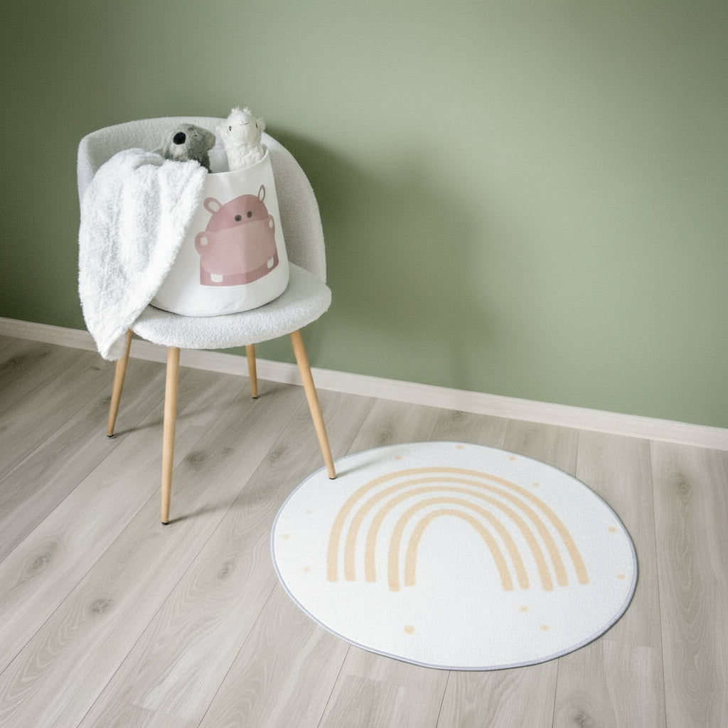 Et rundt teppe med regnbuemotiv som ligger på et gulv, sammen med en stol med barneleker.